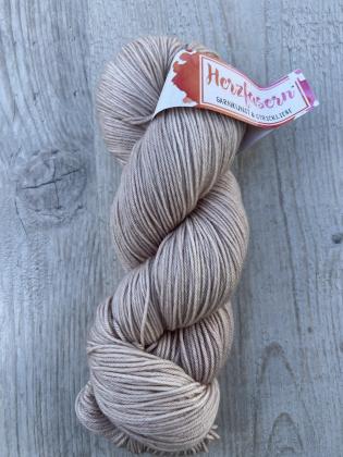 Ein Strang Herzfasern No. 11 (Merino, superfine) in der Farbe Dolomit. Sanftes, steiniges Beige, leicht glänzend, liegt auf einem hellen Holzuntergrund. Das Garn ist locker zu einem klassischen Strang gewickelt, das Herzfasern-Etikett in Pink-Orange ist s